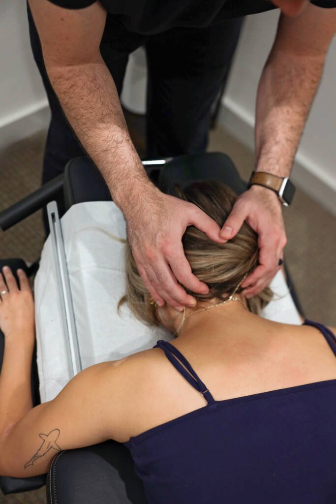 Chiropractor supporting a patient's head and upper neck as she lies face down on a treatment table