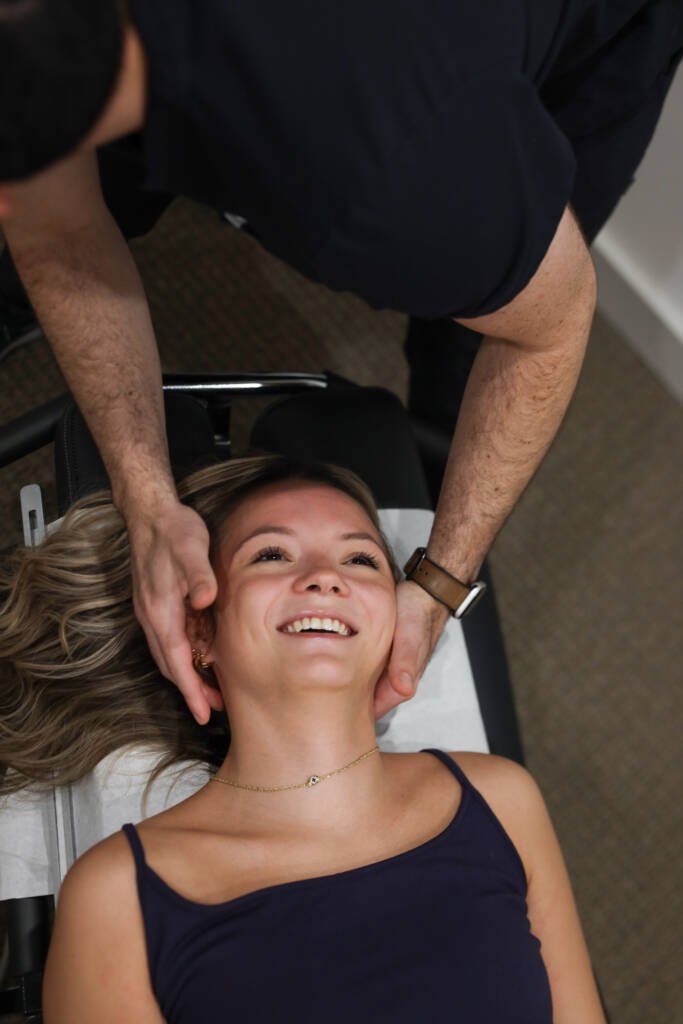 Chiropractor gently cradling a smiling patient's head during neck care while she lies on the treatment table