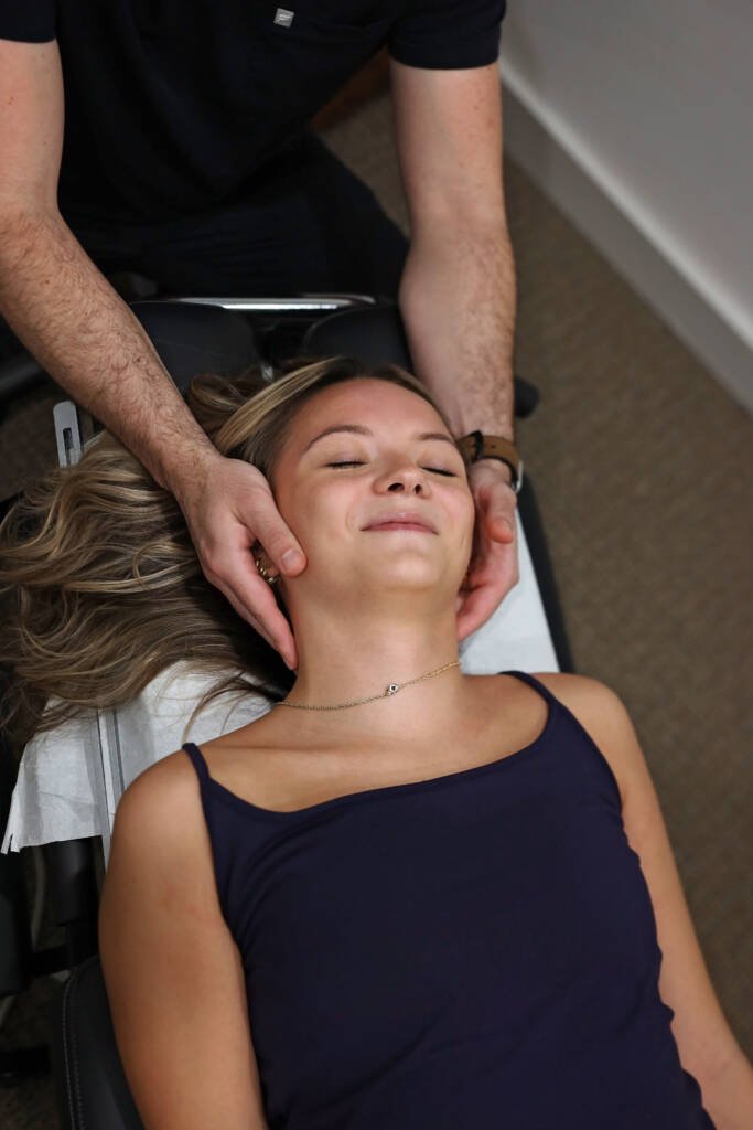 Chiropractor gently assessing a patient's neck as she lies on the treatment table
