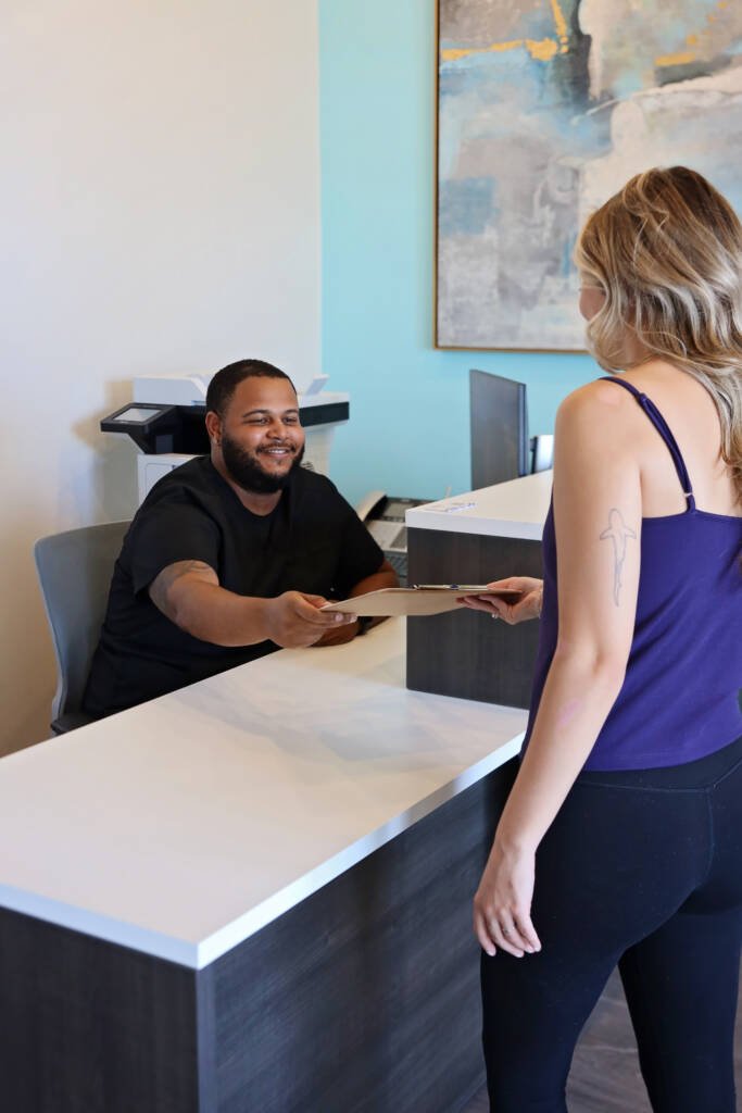 Front desk team member handing a patient paperwork at the reception counter of Urgent Chiropractic of Steele Creek