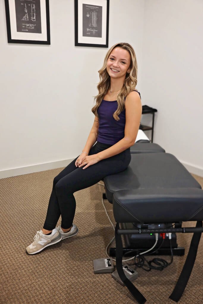 Patient seated on a treatment table in an exam room at Urgent Chiropractic of Steele Creek