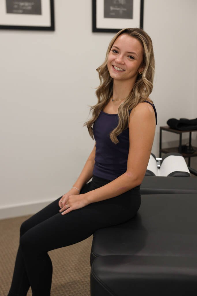 Patient seated on a treatment table at Urgent Chiropractic of Steele Creek before her evaluation