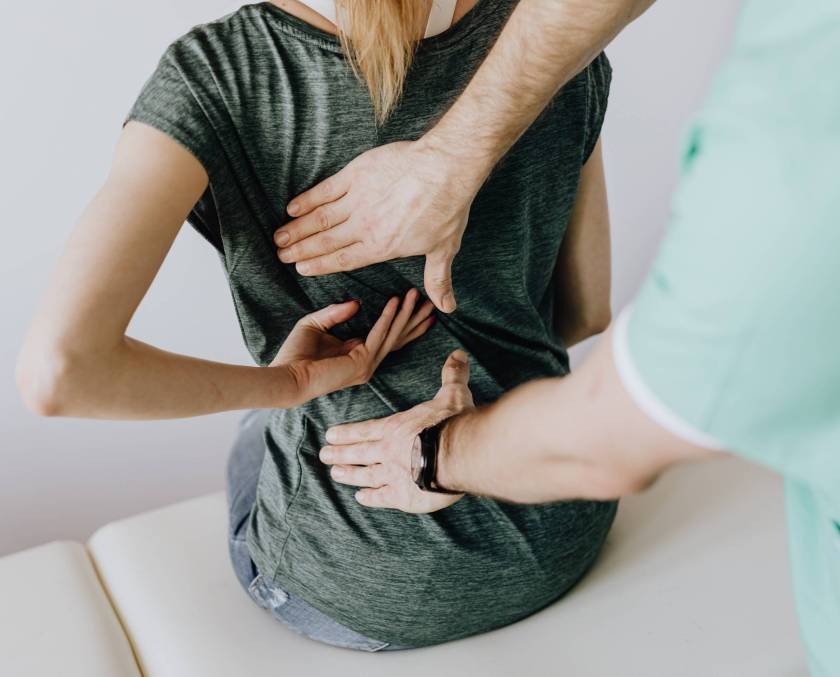 Chiropractor examining a seated female patient's mid and lower back, palpating along the spine with both hands.